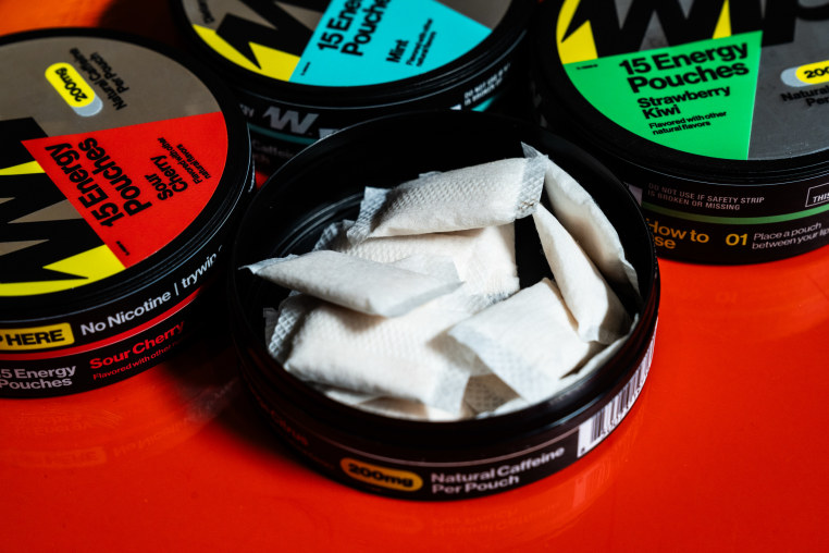 Wip containers displayed on a red table, one of the containers is open and shows white pouches filled with powder inside