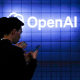 Visitors look at their phone next to an Open AI logo on a blue tiled wall